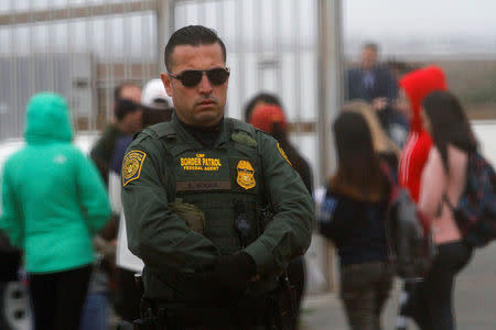 A U.S. Border Patrol agent (C) looks on as people separated by immigration wait to see their relatives at an open gate on the fence along the Mexico and U.S border, as photographed from Tijuana, Mexico February 11, 2017. REUTERS/Jorge Duenes