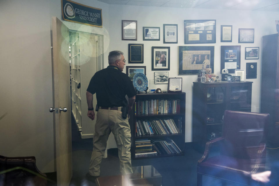 In this image taken through an office window, a law enforcement officer surveys the office of Rep. Gerry Connelly, D-Va., in Fairfax, Va., Monday, May 15, 2023, after police say a man wielding a baseball bat attacked two staffers for Connolly on Monday morning. Fairfax City Police in northern Virginia said in a tweet that a suspect is in custody and the victims are being treated for injuries that are not life-threatening. (AP Photo/Cliff Owen)