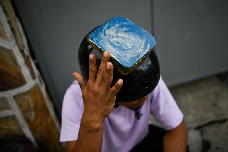 El atleta profesional de breakdance venezolano Kenyer Méndez, de 27 años, coloca una almohadilla de plástico con mantequilla en la parte superior de su casco para deslizarse mejor durante una pausa de su actuación en Caracas