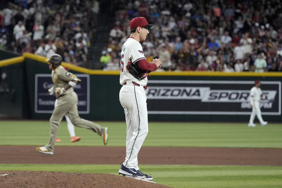 Arizona Diamondbacks relief pitcher Matt Bowman, center, rubs up a new baseball after giving up a two-run home run to San Diego Padres' Manny Machado, left, during the fifth inning of a baseball game Friday, May 3, 2024, in Phoenix. (AP Photo/Ross D. Franklin)