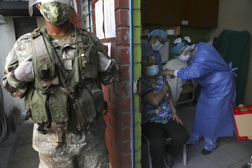 A soldier stands guard as a woman is given a COVID-19 shot