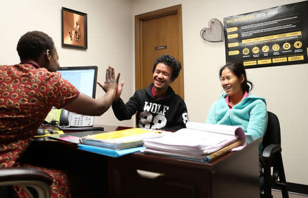 Amy Longa (L) gives Wimber Htoo (middle) a high-five after he gets his new local phone number correct at the IRC office in Garden City, Kansas, U.S., March 26, 2018. REUTERS/Adam Shrimplin