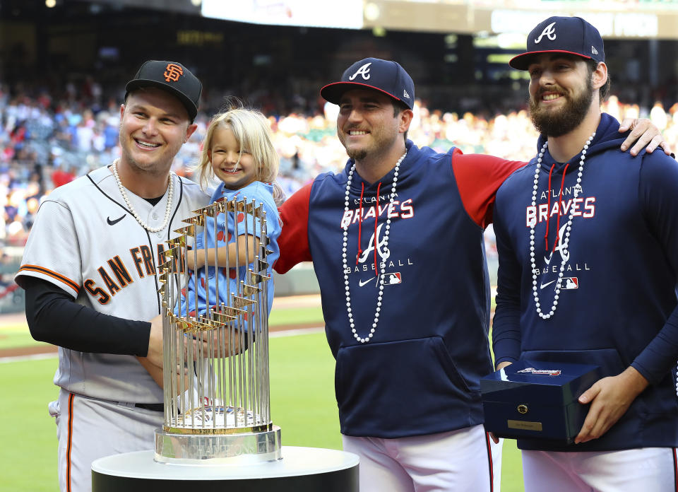 Former Atlanta Braves outfielder Joc Pederson ,left, holds his daughter Poppy as he is presented his World Series ring by Braves pitchers Luke Jackson and Ian Anderson, sporting pearls, before the San Francisco Giants play the Braves in a baseball game on Monday, June 20, 2022, in Atlanta. (Curtis Compton/Atlanta Journal-Constitution via AP)