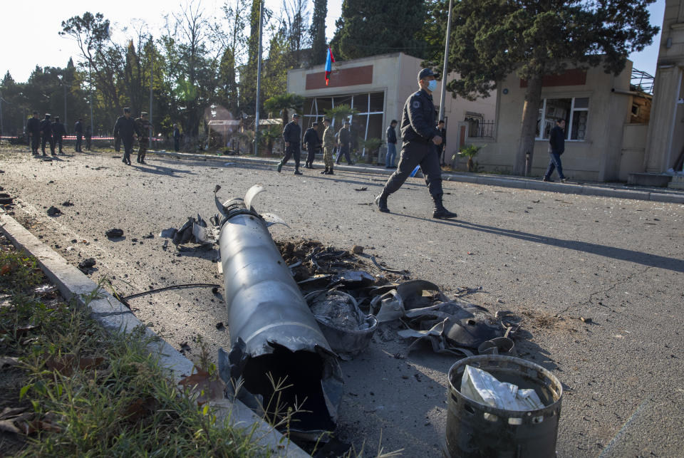 Members of Azerbaijan's security forces, walk past remains of a missile, as they inspect the damage following an overnight missile attack by Armenian forces, in the city of Ganja, Azerbaijan's second-largest city, Thursday, Oct. 8, 2020. The fighting between Armenian and Azerbaijani forces over the separatist territory of Nagorno-Karabakh, continued with both sides accusing each other of launching attacks. The region lies in Azerbaijan but has been under the control of ethnic Armenian forces backed by Armenia since the end of a separatist war in 1994. (Unal Cam/DHA via AP)