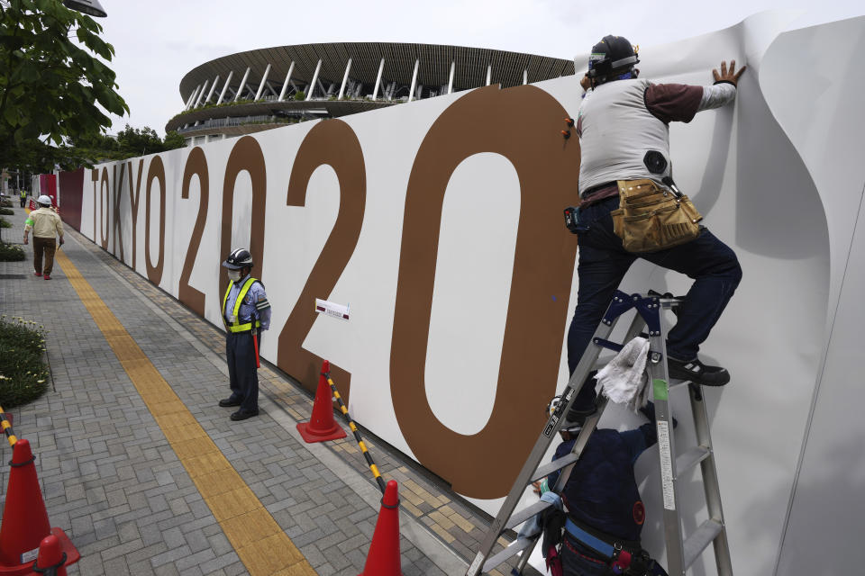 FILE - In this June 2, 2021, file photo, workers paste the overlay on the wall of the National Stadium, in Tokyo. The Tokyo Olympics are not looking like much fun: Not for athletes. Not for fans. And not for the Japanese public, who are caught between concerns about the coronavirus at a time when few are vaccinated on one side and politicians and the International Olympic Committee who are pressing ahead on the other. (AP Photo/Eugene Hoshiko, File)