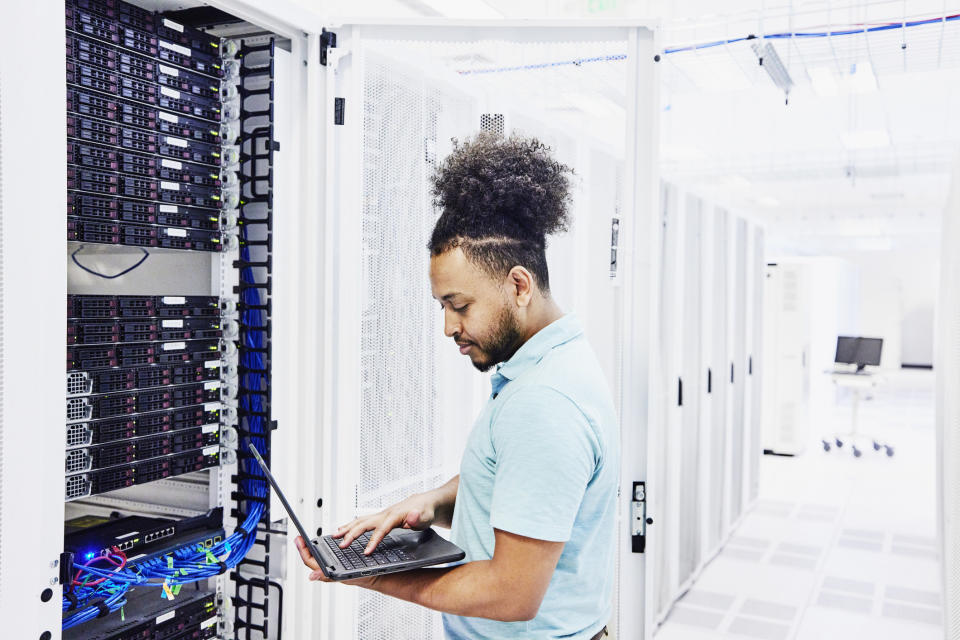 IT professional looking at laptop while working on server in data center