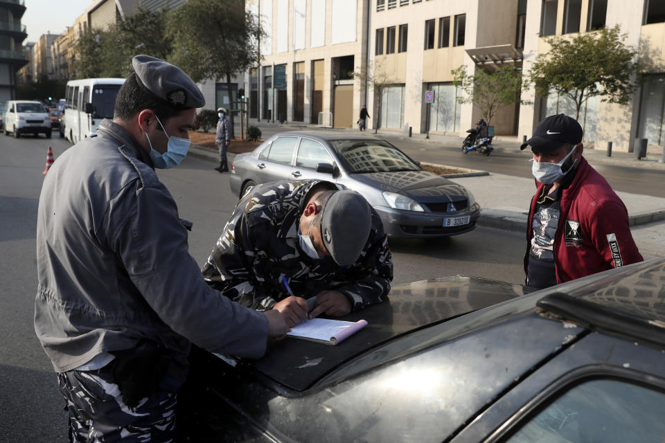 A police officer issues fines to owners of vehicles that violate the odd and even license plate rule on alternating days as the country begins a three-week lockdown to limit the spread of coronavirus amid a post-holiday surge in the past 10 days in Beirut, Lebanon, Thursday, Jan. 7, 2021. (AP Photo/Bilal Hussein)