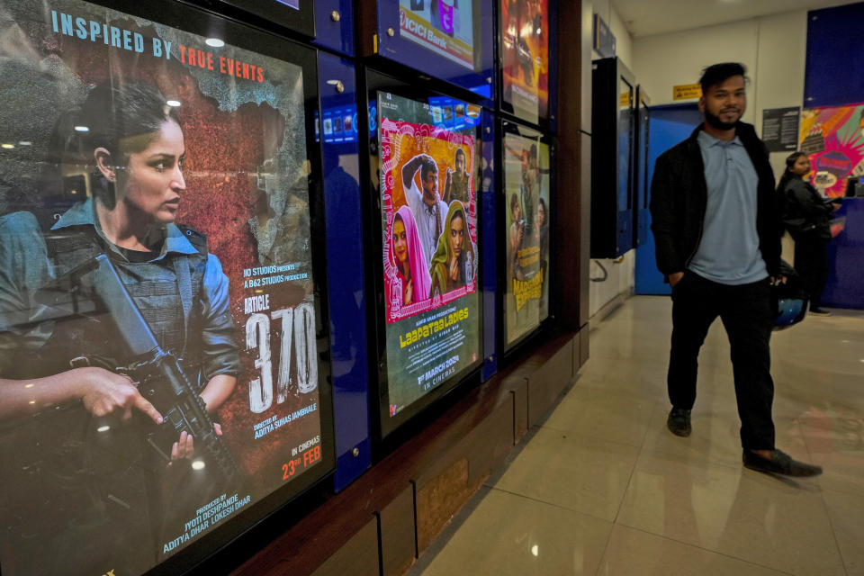 A man stands next to a poster of the movie Article 370 displayed at a cinema hall in Guwahati, India, Thursday, March 21, 2024. The movie is one of several upcoming Bollywood releases based on polarizing issues, which either promote Indian Prime Minister Narendra Modi and his government’s political agenda, or lambast his critics. (AP Photo/Anupam Nath)