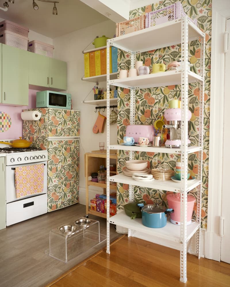 White industrial storage unit filled with kitchen wares on wallpapered wall beside kitchen.