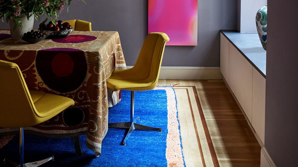 long pink artwork on a dusky purple wall with a draped table in front with yellow swivel chairs pulled up to it