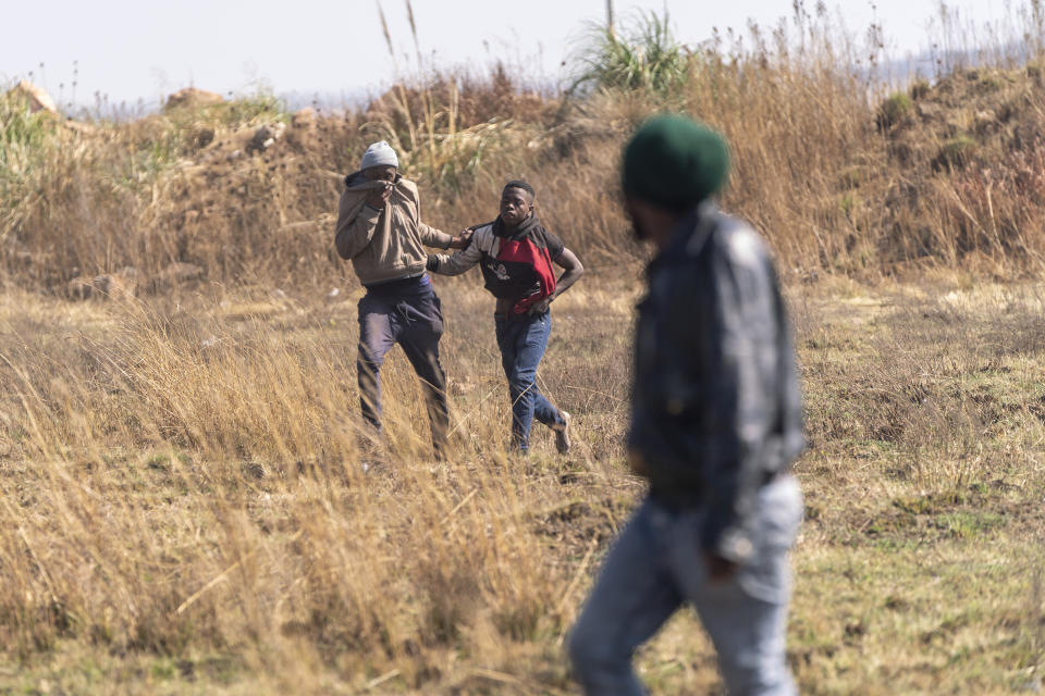 CORRECTS AS IMAGE DOES NOT SHOW PEOPLE RUNNING FROM TEAR GAS AND STUNT GRENADES - A resident, left, grabs a man suspected of being an illegal miner in the South African city of Krugersdorp Thursday Aug. 4, 2022. Community members in the assaulted suspected illegal miners and set fire to their camps on Thursday in an outpouring of anger following the alleged gang rapes of eight women by miners last week. Residents of Krugersdorp's Kagiso township also barricaded roads with rocks and burning tires during a planned protest. (AP Photo/ Shiraaz Mohamed)