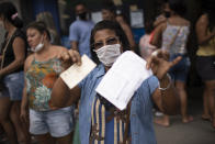Manicurist Severina de Almeida shows her documents as she waits outside a government-run bank having technical problems to distribute aid money to people without work amid the new coronavirus pandemic's affect on the economy in Rio de Janeiro, Brazil, Tuesday, April 28, 2020. (AP Photo/Silvia Izquierdo)