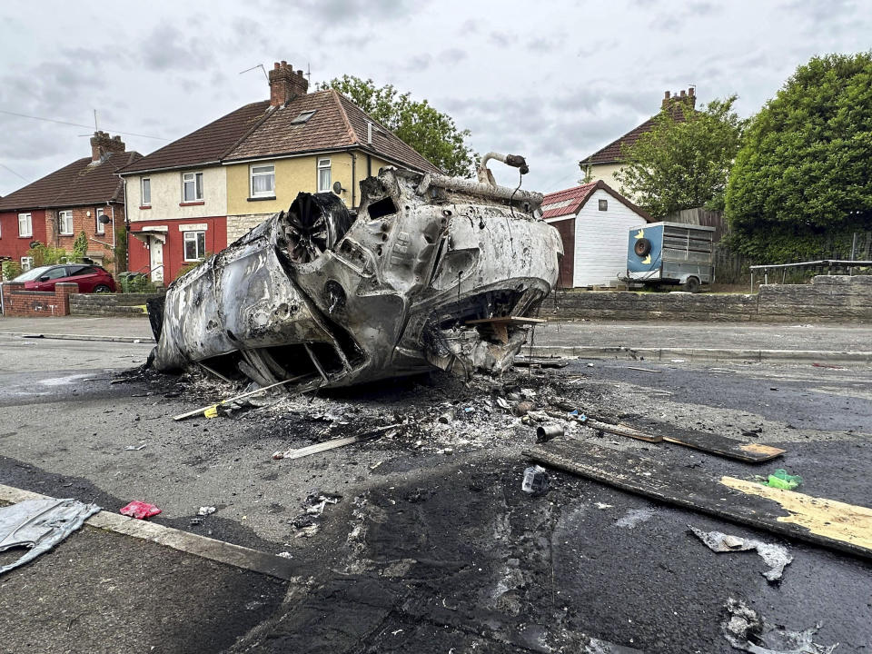 A burnt vehicle is seen at the scene where a riot broke out after two teenagers died in a crash, in Ely, Cardiff, Tuesday May 23, 2023. Several dozen youths pelted police with objects and set cars ablaze on Monday evening in Cardiff in local unrest that erupted after two teenagers died in a road accident. (PA via AP)