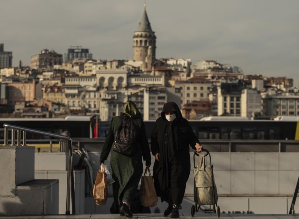 Backdroped by Istanbul's iconic Galata Tower women, one wearing a mask as a preventive measure against the spread of coronavirus, walk in Istanbul, Friday, April 17, 2020, just hours before the start of a two-day curfew declared by Turkey's government in an attempt to control the spread of coronavirus. (AP Photo/Emrah Gurel)