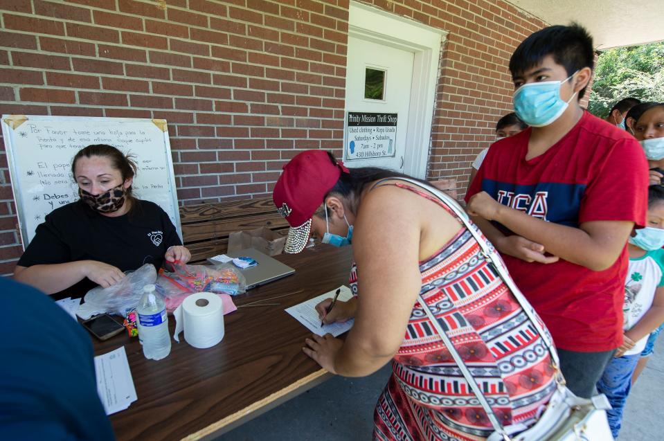 Adelaida Gabriel (center), of Forest, Miss., and her son Alexis, 14 (right), check in with Monica Soto with El Pueblo, a nonprofit specializing in immigration legal services, before picking up school supplies during a distribution at Trinity Mission Center in Forest, Miss., Saturday, July 11, 2020. Gabriel is still wearing an ankle bracelet since the August 2019 ICE raids at local poultry processing plants but she didn't want to talk about the past year when her son asked her. He said she replied, "It makes her sad."