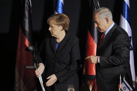 German Chancellor Angela Merkel holds her crutches as Israel's Prime Minister Benjamin Netanyahu (R) stands next to her after their joint news conference in Jerusalem February 25, 2014. Germany views Iran as a potential threat not just to Israel, but also to European countries, Merkel said on Tuesday at a joint news conference with Netanyahu. REUTERS/Ammar Awad