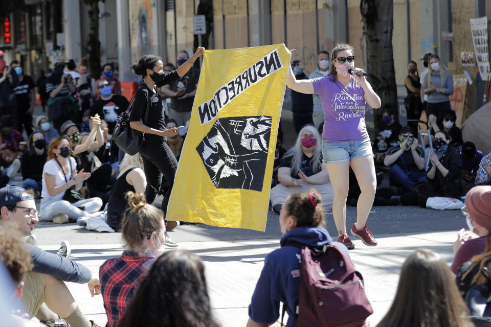 Protesters display a flag that they said flew over a protest camp during Seattle's World Trade Organization protests in 1999 as they speak at a rally in front of the Seattle Police Department East Precinct building, which has been boarded up and abandoned except for a few officers inside, Thursday, June 11, 2020, inside what is being called the "Capitol Hill Autonomous Zone" in Seattle. Following days of violent confrontations with protesters, police have largely withdrawn from the neighborhood. (AP Photo/Ted S. Warren)