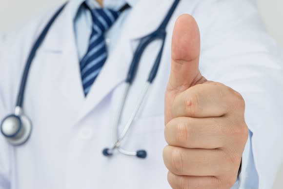 A doctor with a stethoscope around his neck giving the thumbs-up sign.