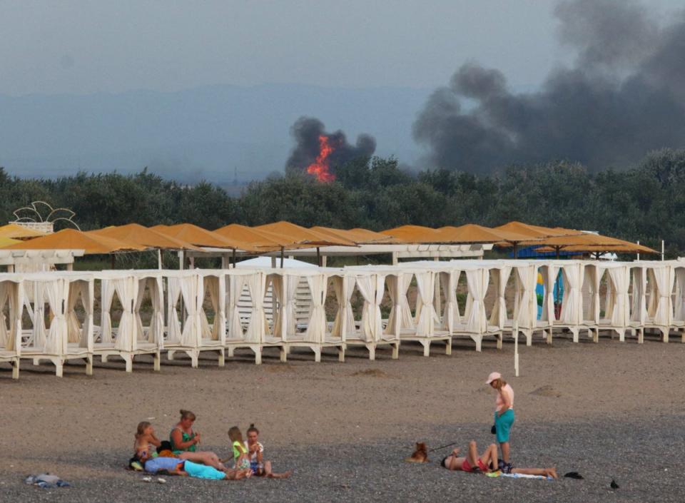 People rest on a beach as smoke and flames rise at a Russian military base (REUTERS)