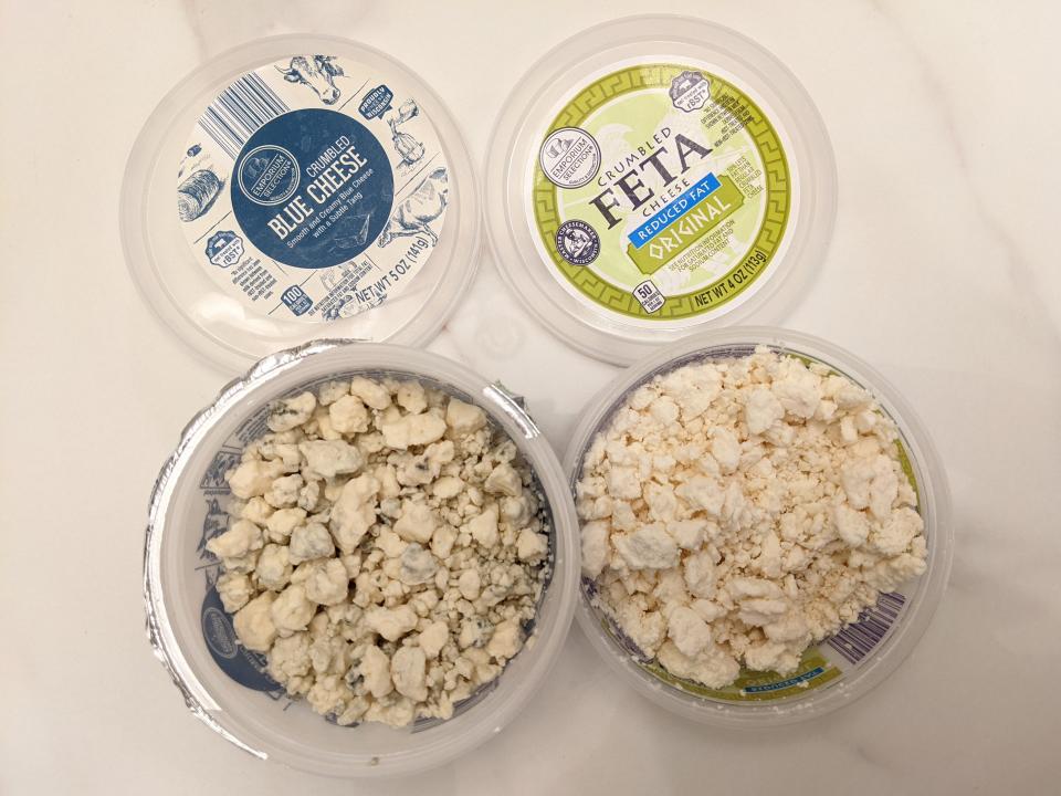 Aldi blue cheese and feta crumbles in their original plastic containers on a white countertop