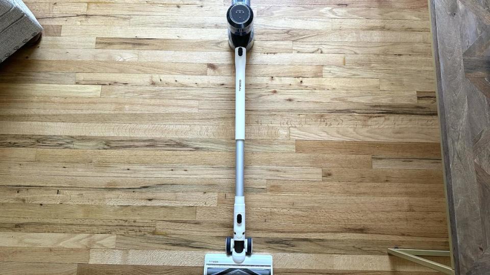 Photo of a stick vacuum lying on a wood-tiled floor.