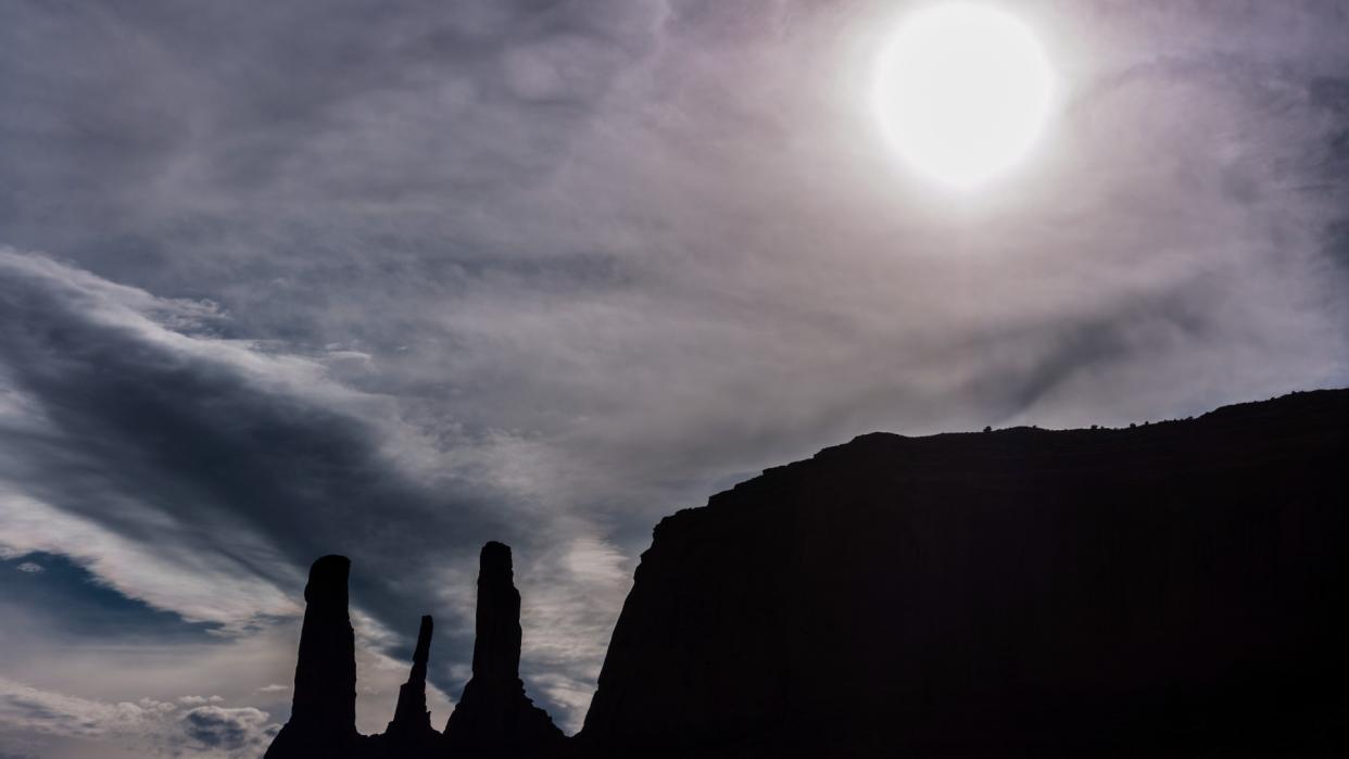  The sun can be seen in the sky above three tall spires of rock in the desert. 
