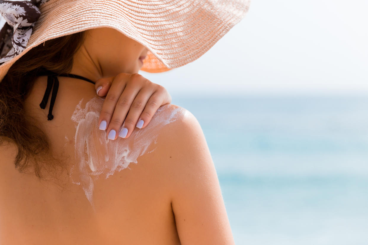 Young girl in straw hat is applying sunscreen on her back to protect her skin.