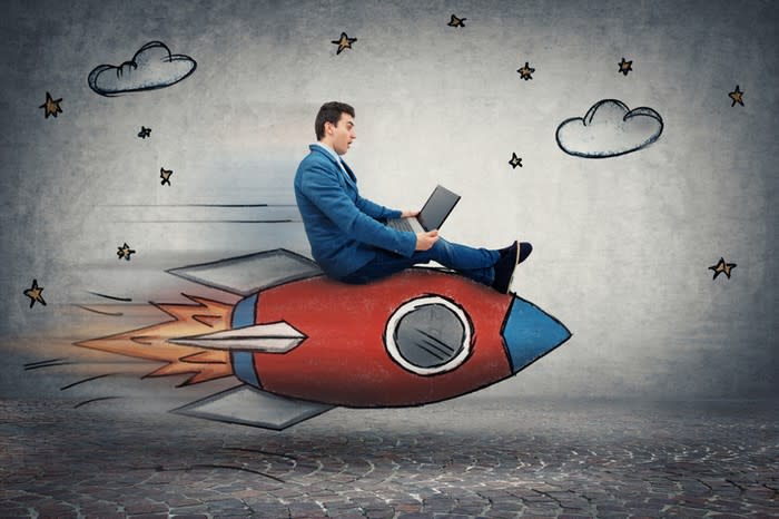 A businessman viewing his laptop while sitting on a cartoon rocket.