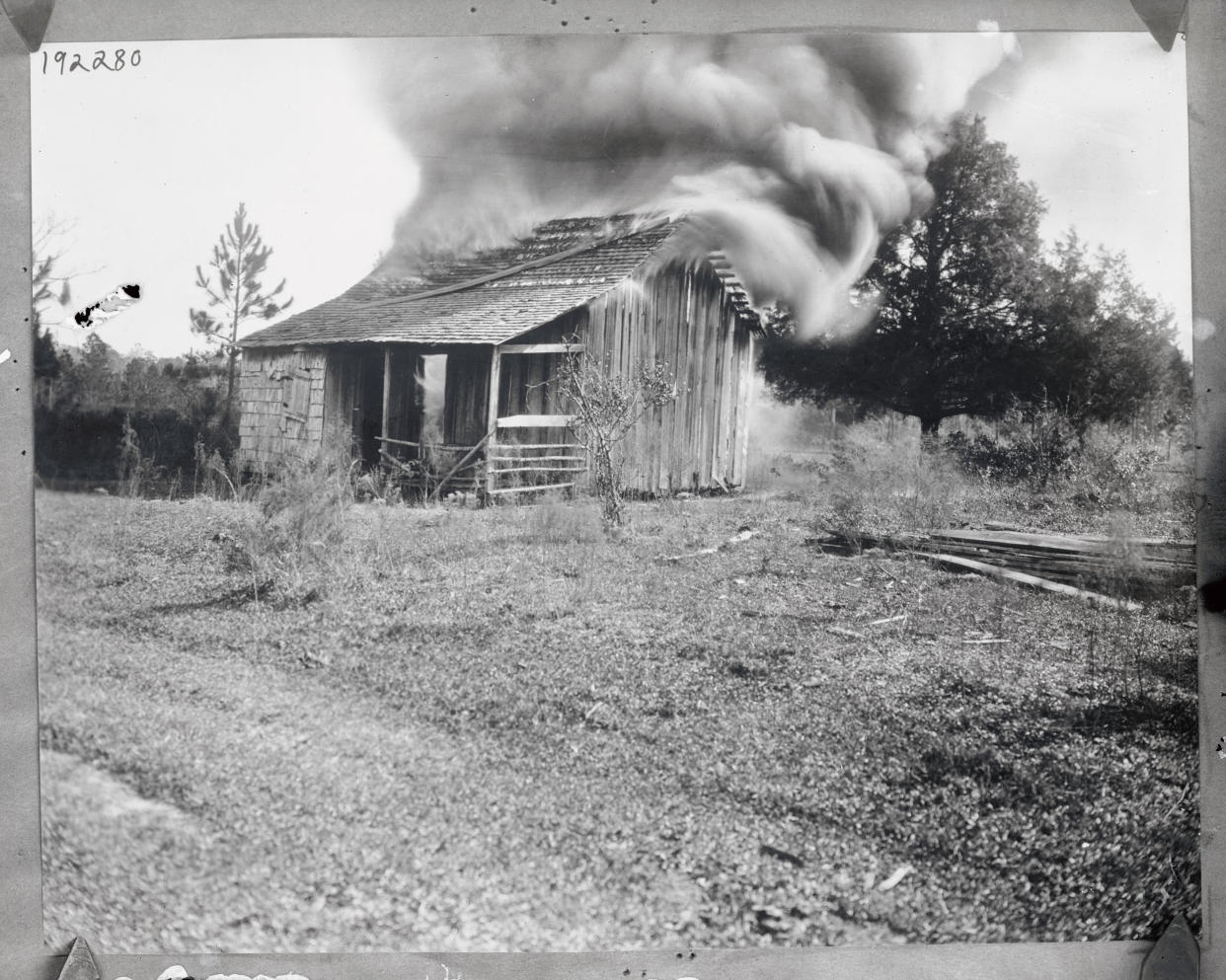 A black-and-white photo of a small house that is on fire.