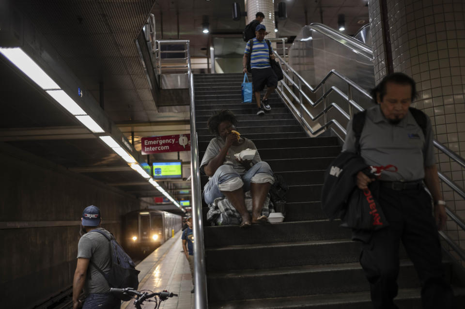 Commuters walk down the steps to board a Metro train as a homeless woman eats her food in Los Angeles, Tuesday, Sept. 19, 2023. Billions of dollars have been spent on homelessness in the region, and an array of new programs are in place. But Mayor Karen Bass says it's possible that the number of homeless people will continue to increase, in part because of evictions and the end of pandemic aid that helped pay bills for lower-income households. (AP Photo/Jae C. Hong)