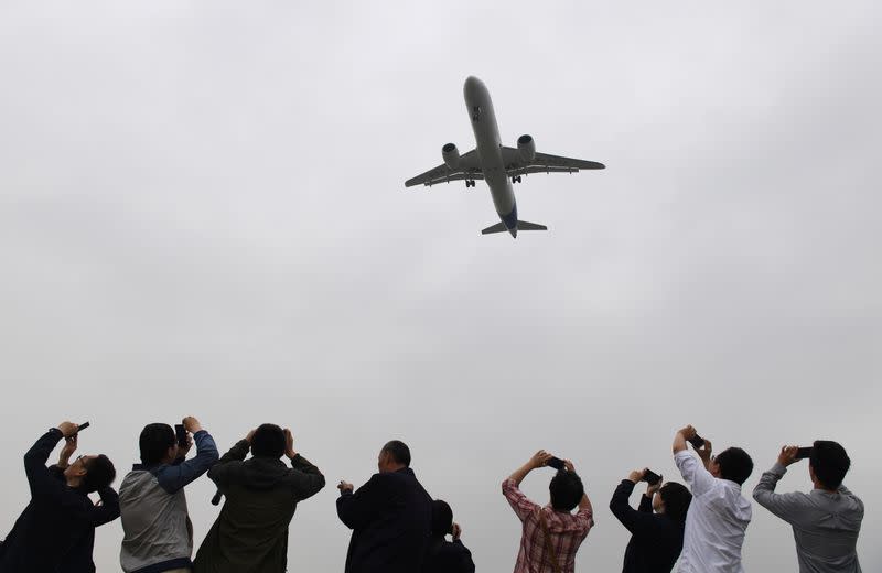 Spectators take photos as they watch the Comac C919, China's first large passenger jet, coming in for a landing on its maiden flight at Shanghai's Pudong airport