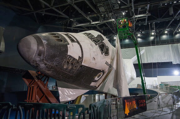 Construction workers at the Kennedy Space Center Visitor Complex in Florida carefully remove a section of plastic shrink wrap from the space shuttle Atlantis inside the $100 million exhibit dedicated to the retired NASA orbiter, April 25, 2013.