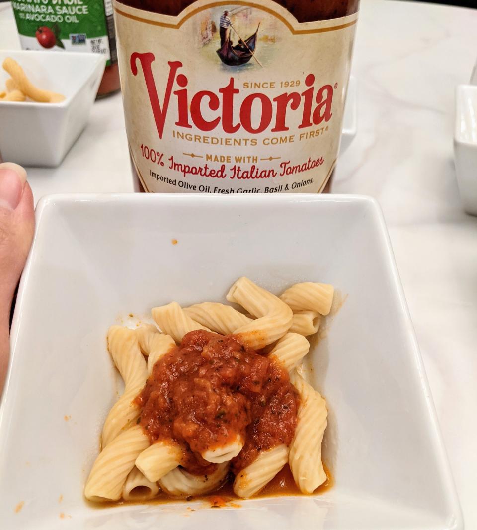 jar of victoria red sauce behind a small white bowl of pasta