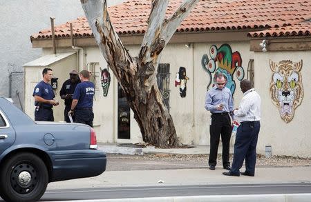 Police confer near a tattoo parlor at one of the scenes of a multiple location shooting that has injured at least four people in Mesa, Arizona March 18, 2015. REUTERS/Deanna Dent