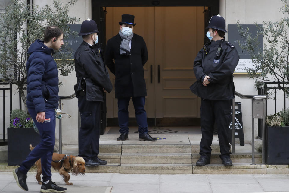 Un hombre pasa con su perro frente al hospital King Edward VII, donde policías resguardan una entrada el martes 23 de febrero de 2021. El príncipe Felipe de Inglaterra ingresó al hospital privado el martes 16 de febrero tras sentirse enfermo. El Palacio de Buckingham dijo el martes 23 de febrero que el esposo de la reina Isabel II era atendido por una infección. (AP Foto/Kirsty Wigglesworth)