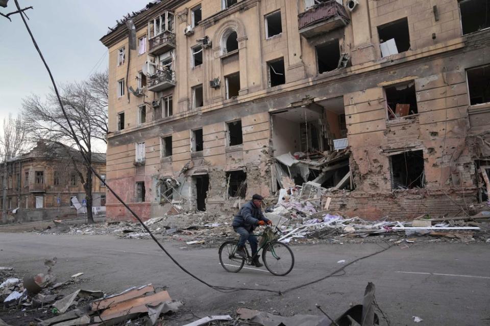 A man rides a bicycle in front of a damaged by shelling apartment building in Mariupol, Ukraine, Wednesday, March 9, 2022. (AP)