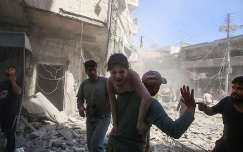 A man evacuates a girl after a reported air strike by regime forces and their allies in the rebel-held Syrian town of Ma`arat al-Nu`man in the southern Idlib province - Credit: AFP