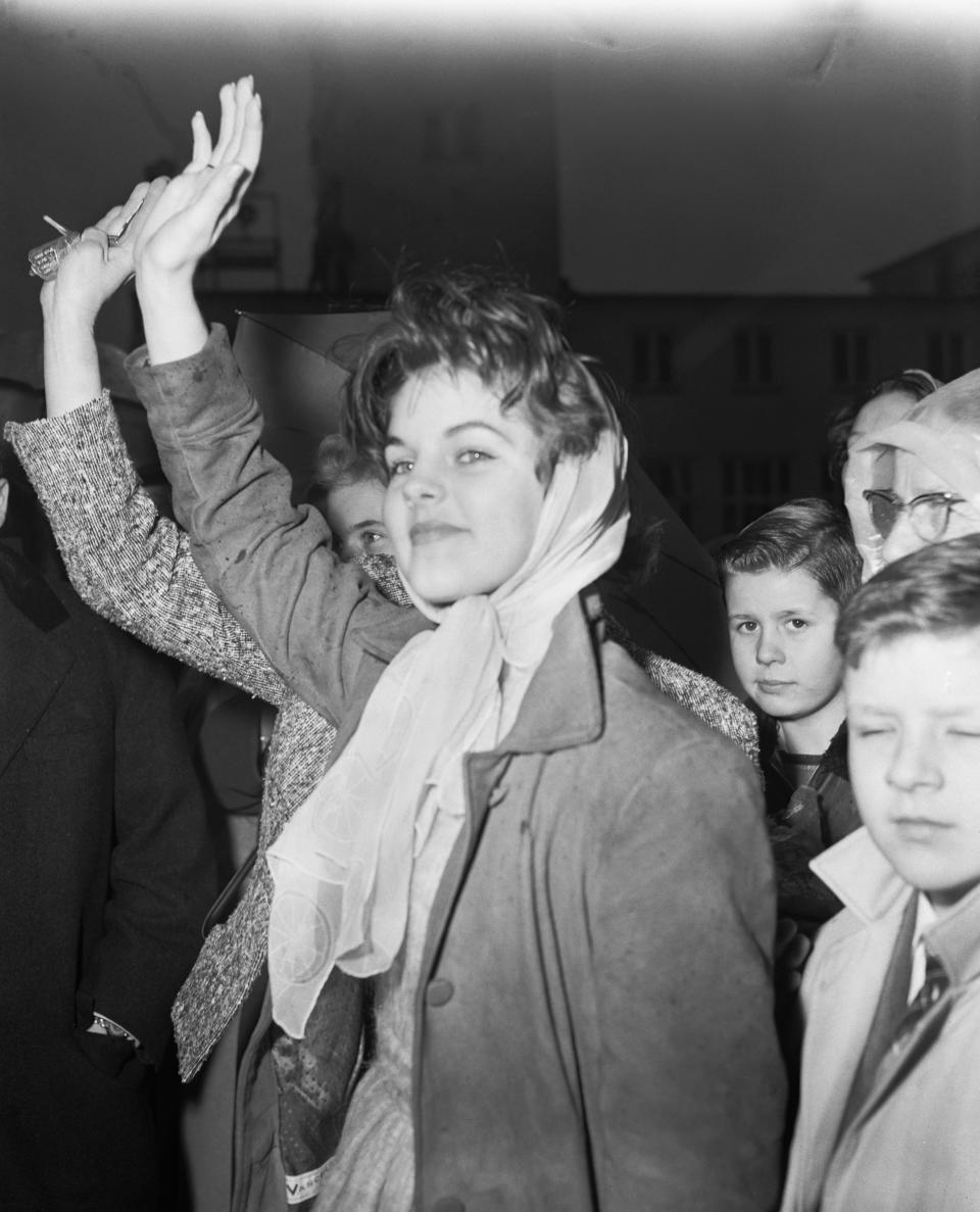 Priscilla smiling and waving with people behind her