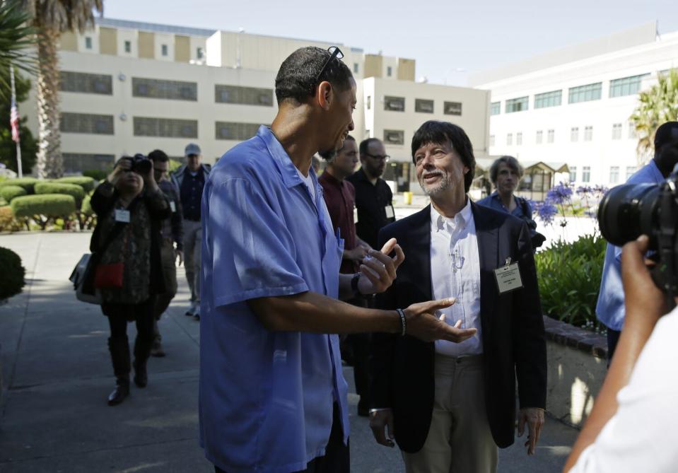 Two men converse, one in jail clothing and the other with an identification badge on his sports coat pocket