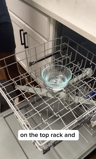 Dishwasher open with one glass on the top rack and overlay text