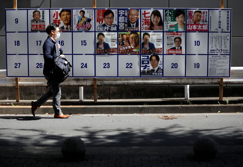 A passerby wearing a protective face mask walks past candidate posters, including current governor Yuriko Koike, for the upcoming Tokyo governor election during the spread of the coronavirus disease (COVID-19), in Tokyo