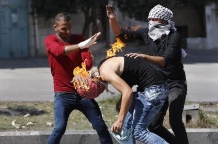 Palestinian protesters put out a fire burning on a compatriot, caused by a molotov cocktail which he was trying to hurl at Israeli troops during clashes in the West Bank city of Hebron, October 13, 2015. REUTERS/Mussa Qawasma