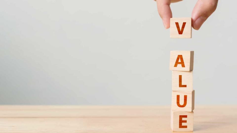 Person's hand putting a wooden cube block with the word VALUE on a wooden table