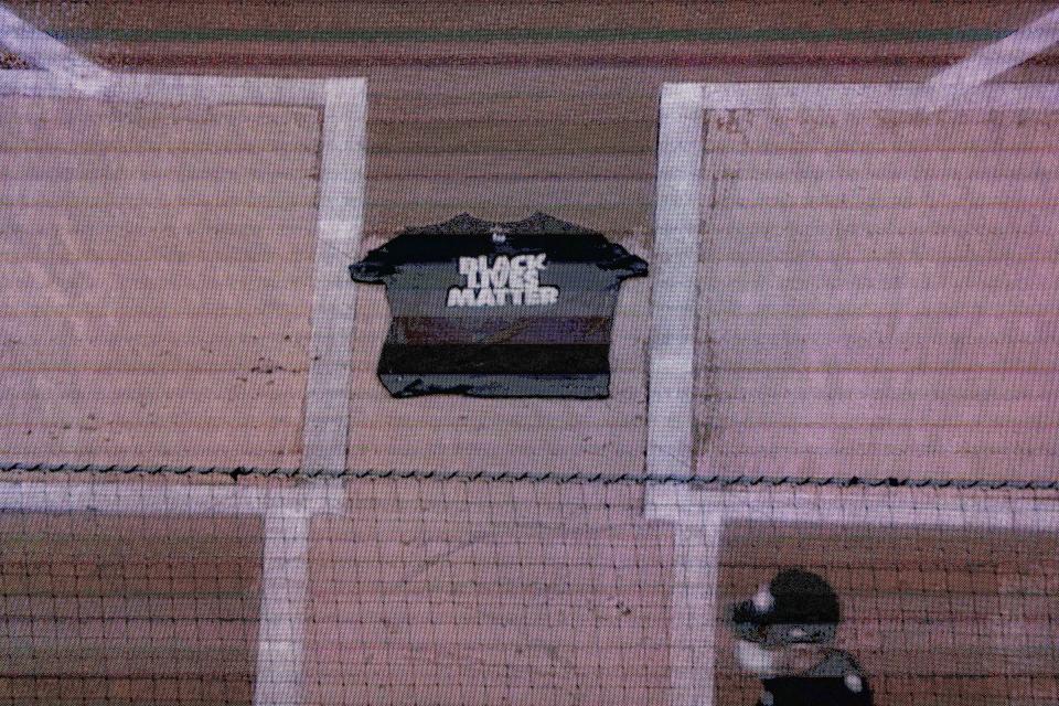 An umpire passes a Black Lives Matter shirt placed on home plate by Miami Marlins center fielder Lewis Brinson as it is displayed on the centerfield screen after they and the New York Mets walked off the field in protest at the start of their baseball game, Thursday, Aug. 27, 2020, in New York. (AP Photo/John Minchillo)