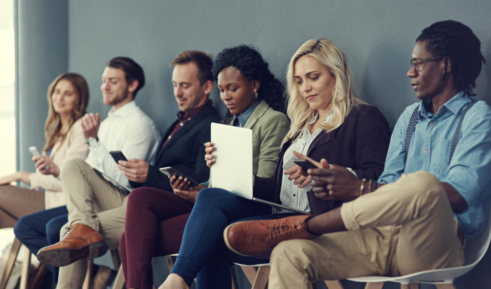 Shot of a group of businesspeople using different wireless devices while waiting in line for an interview