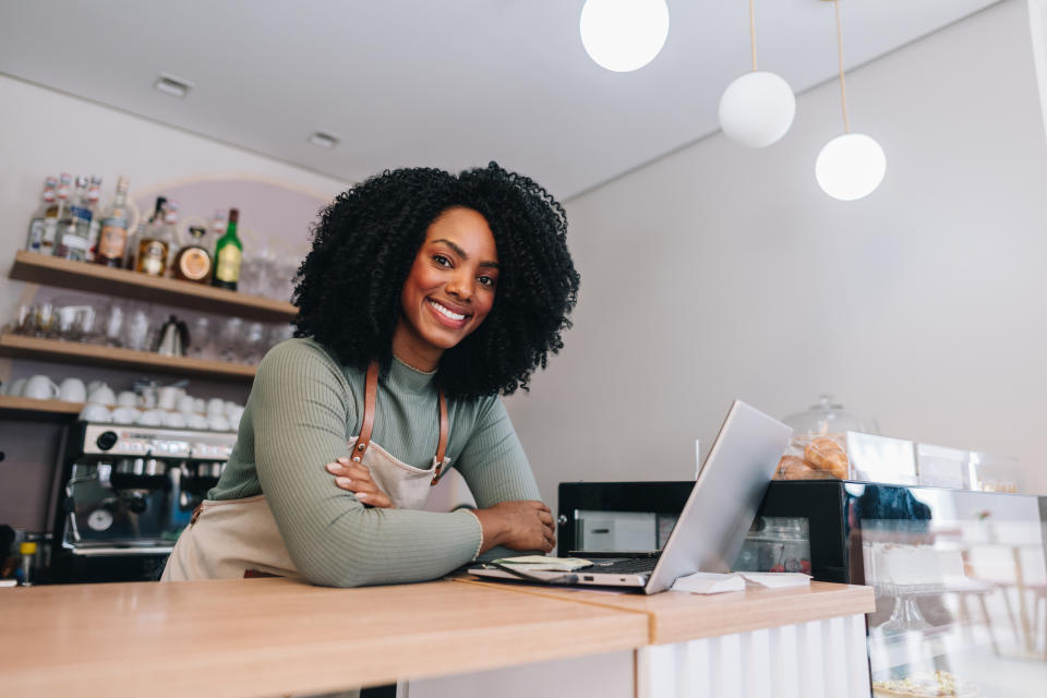 Smiling woman at cafe counter with a laptop and pastries display