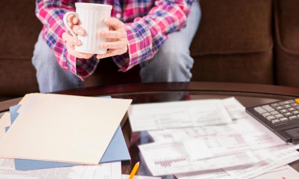 Woman sitting on sofa with large pile of invoices on coffee table in front of her.