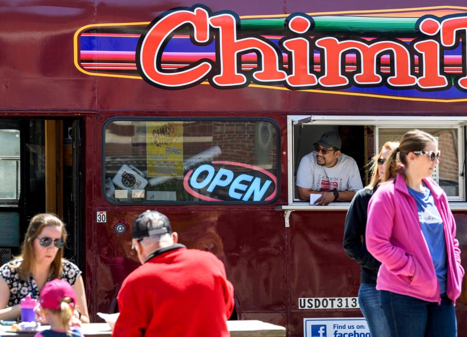 Tacoholics owner Marcos Nicolas, center, watches people walk by the restaurant's double-decker "ChimiTruck" bus during the first day of the 32nd annual Tri-Fest in downtown Henderson, Ky., Friday, April 26, 2019. The ChimiTruck features seating on the second level that can be used by Tri-Fest visitors this weekend. 