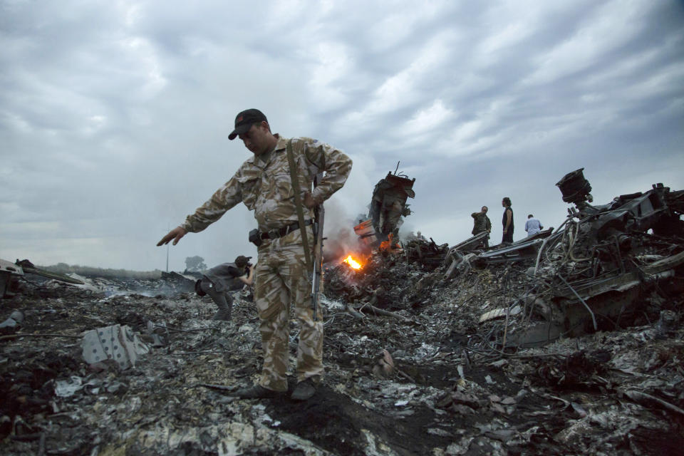 FILE - In this July 17, 2014. file photo, people walk amongst the debris at the crash site of MH17 passenger plane near the village of Grabovo, Ukraine, that left 298 people killed. An international team of investigators piecing together a criminal case in the July 2014 shooting down Malaysia Airlines Flight 17 over eastern Ukraine said Thursday Nov. 14, 2019, that evidence suggests links between Russia and rebels in the region were closer than previously believed.(AP Photo/Dmitry Lovetsky, File)