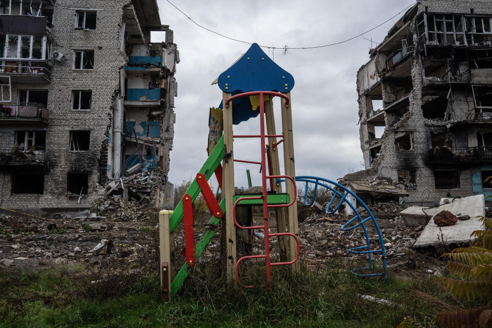 An apartment block that was destroyed by Russian occupying forces looms over a children's play area.